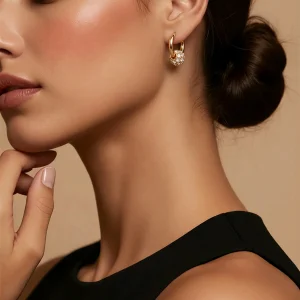 Close up of a woman wearing gold crystal ball huggie hoop earrings with a pave crystal charm.