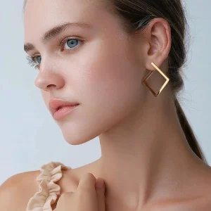 Close up of a woman wearing gold stainless steel open square geometric hoop earrings.